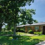 A front view of 5703 Sutherlin with a shady yard and red brick home and a red stone pathway leading to the front door.