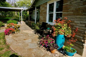 View of a stone pathway lined with turquoise colored flower pots and orange and pink flowers.