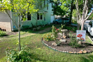 A side view of the house with a rock lined flower bed where you'll find a bird bath and red knockout roses.